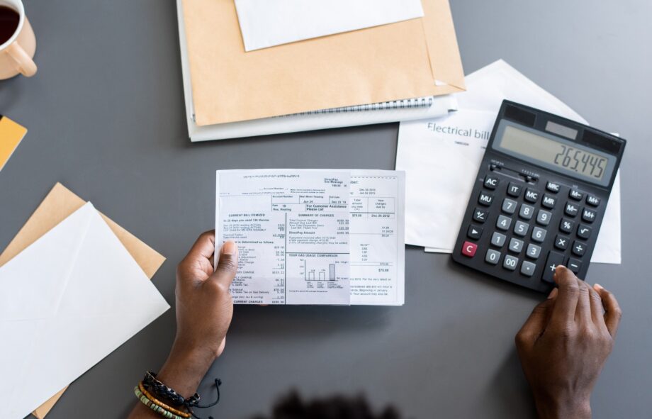 Directly above view of blackman sitting at gray table with letters and making calculations while examining bills